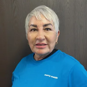 smiling woman with a blue merry maids uniform standing in front of a tan wall